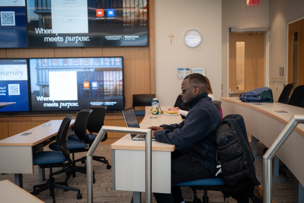 Two students type on their laptops in a classroom