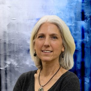 A woman smiles in front of a blue and white textured background