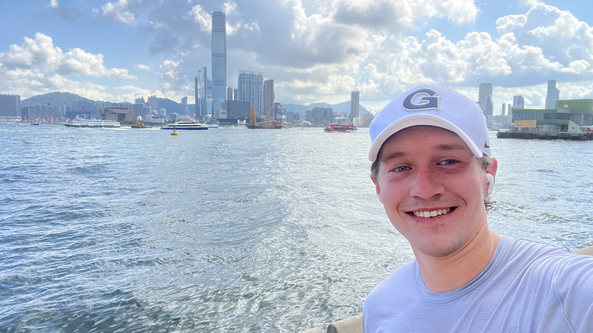 Young Caucasian man in GU hat standing in front of a bay on a sunny day