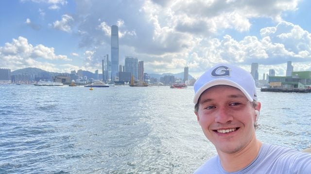 Young Caucasian man in GU hat standing in front of a bay on a sunny day