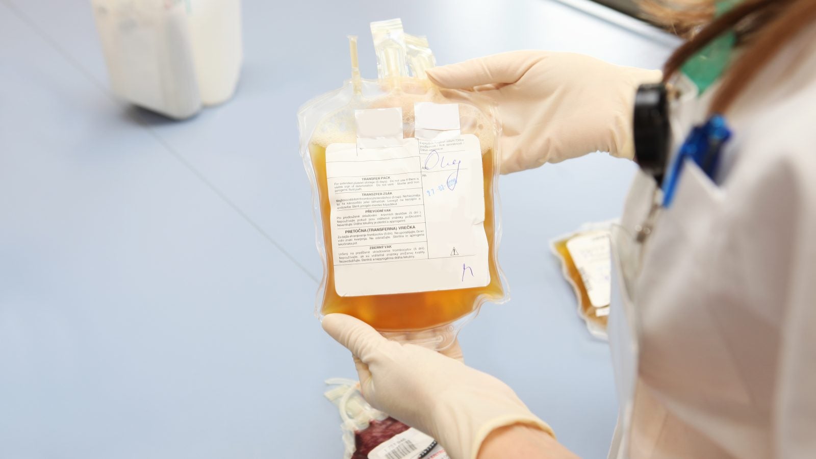A medical professional holds a yellow bag of blood plasma