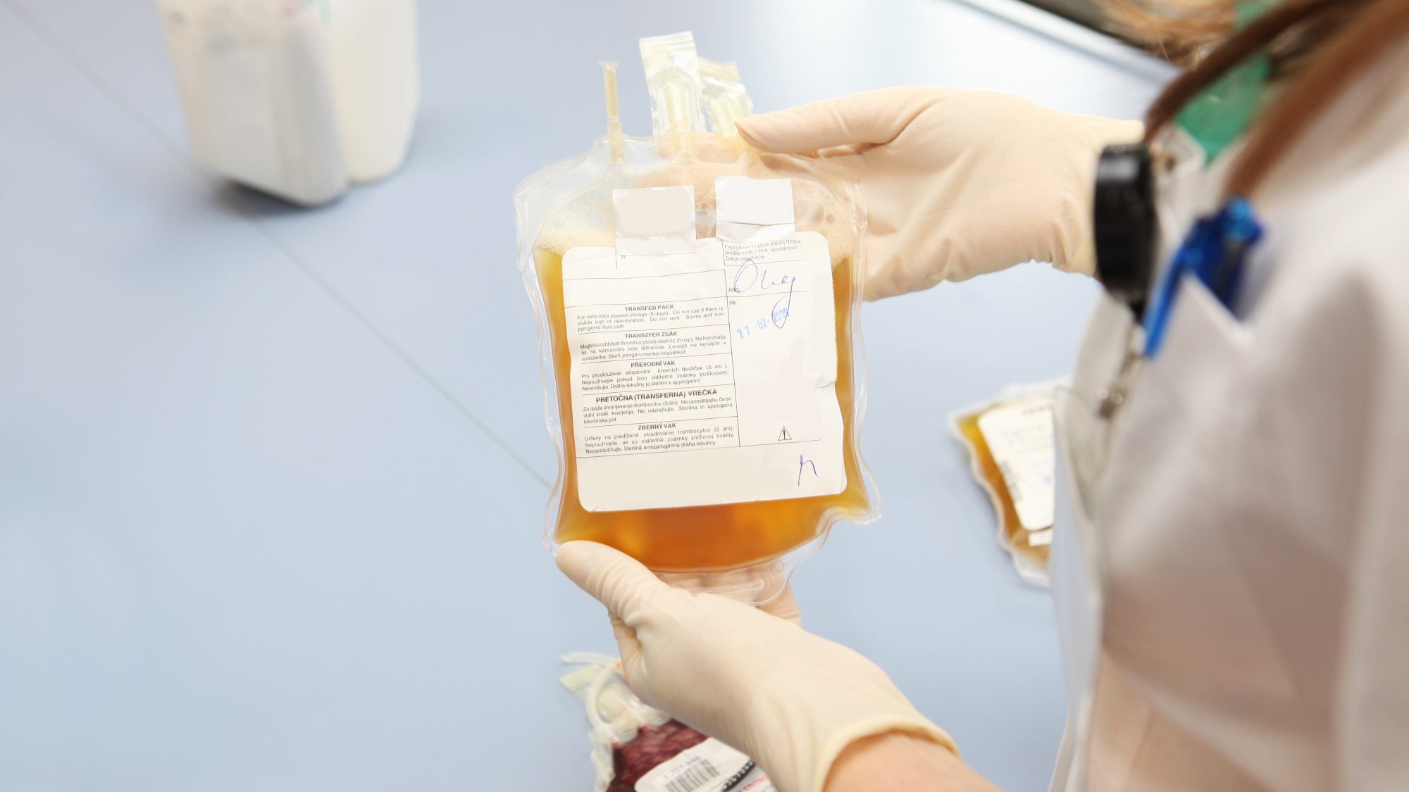 A medical professional holds a yellow bag of blood plasma