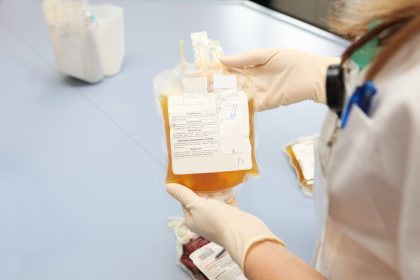 A medical professional holds a yellow bag of blood plasma