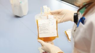 A medical professional holds a yellow bag of blood plasma
