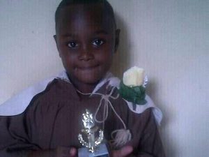 A slightly blurry photo of a baby boy with a rose on his shoulder holding a trophy