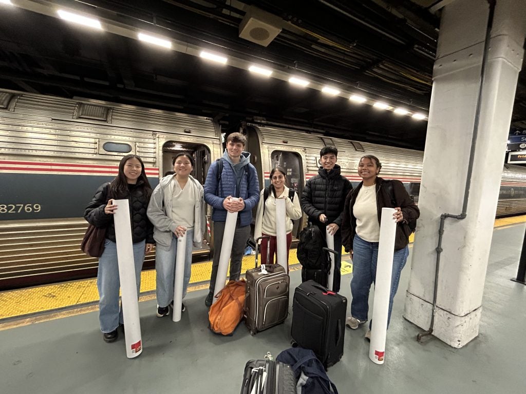 A group of students stand holding posters outside of an Amtrak train inside a station