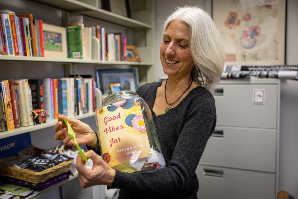 A woman holds a jar that says "Good Vibes Jar" and smiles