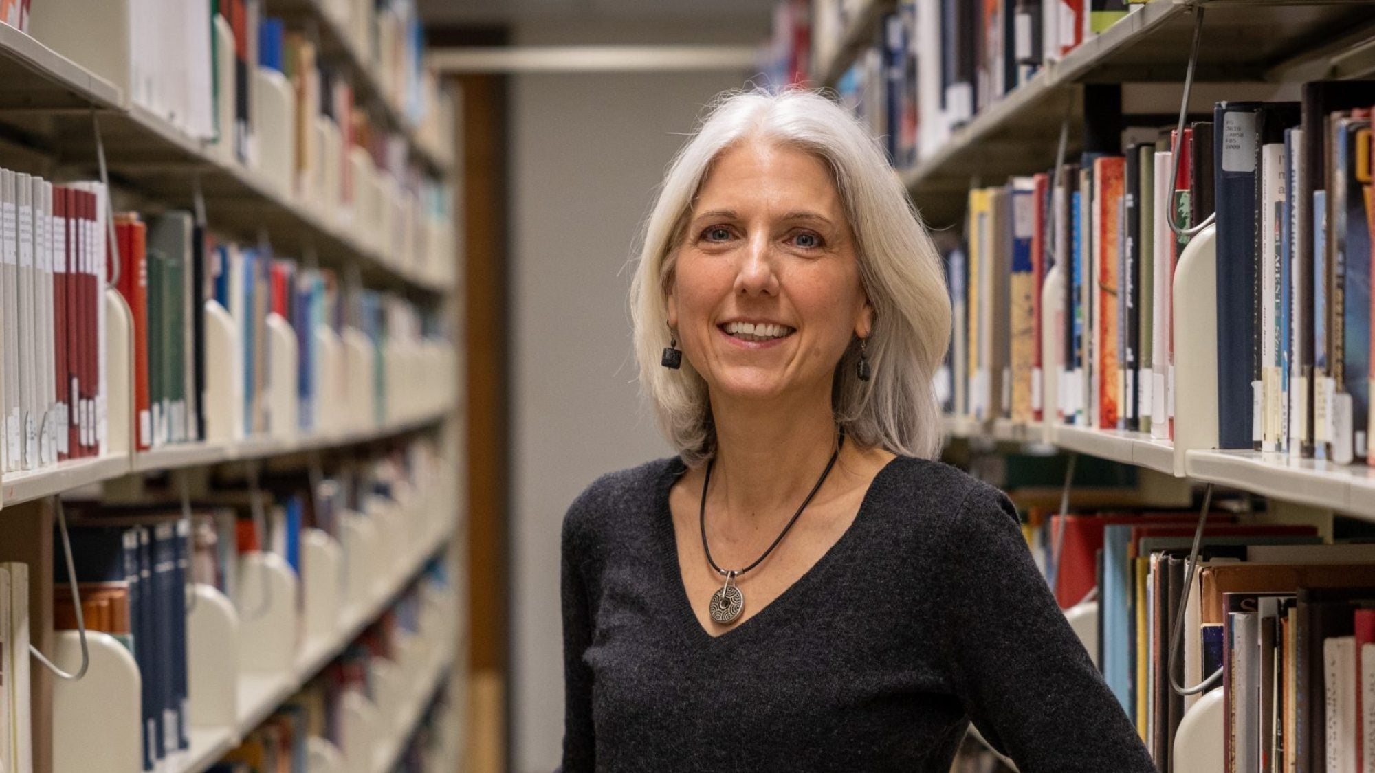 A woman stands in an aisle of book shelves in a library