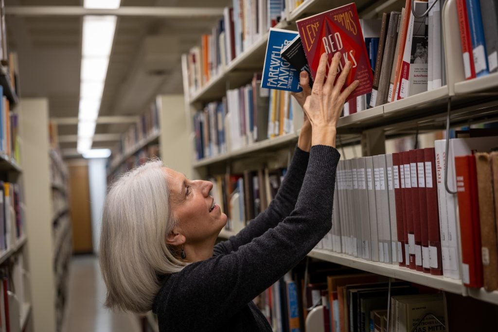 A woman picks up books from a library shelf