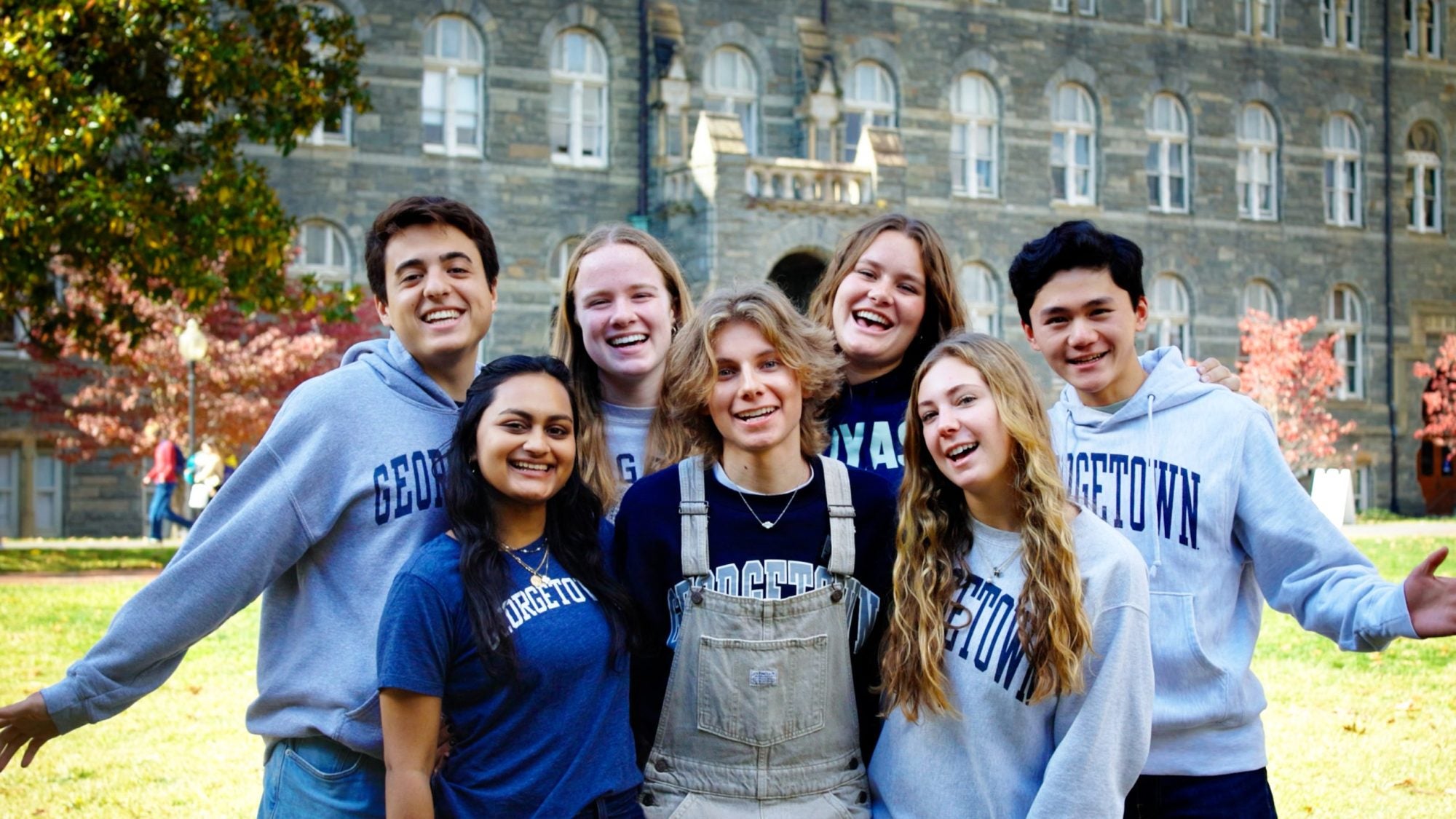 Students in Georgetown gear huddle and smile in front of Healy