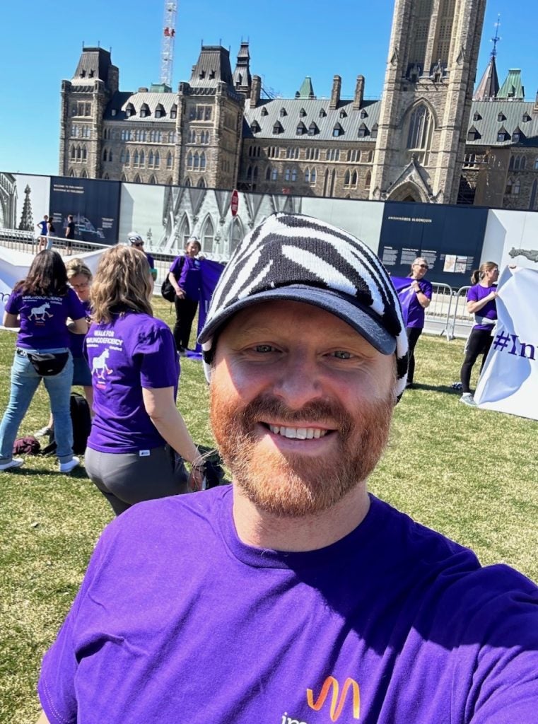 A man in a purple T-shirt and zebra hat poses during a nonprofit event