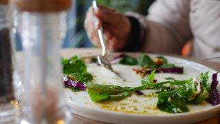 A diner finishes eating a salad on a white plate