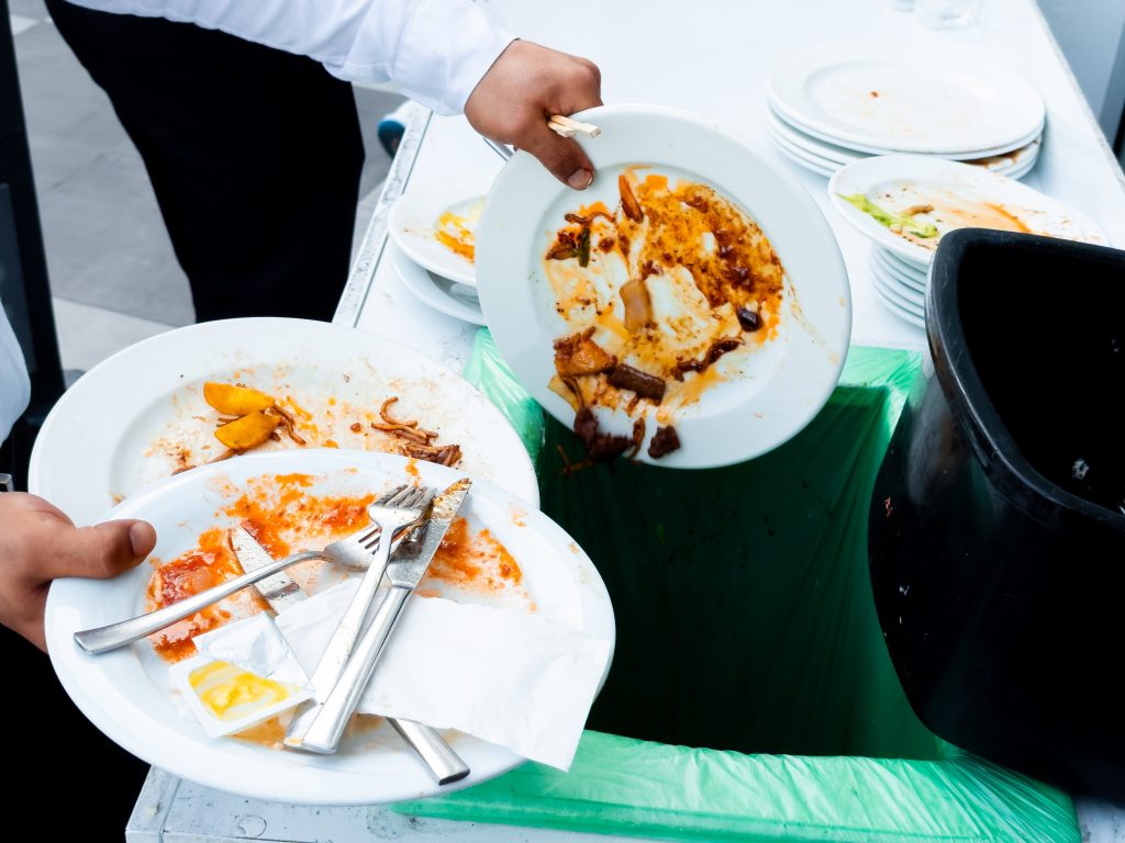 A server throws away uneaten food on white plates
