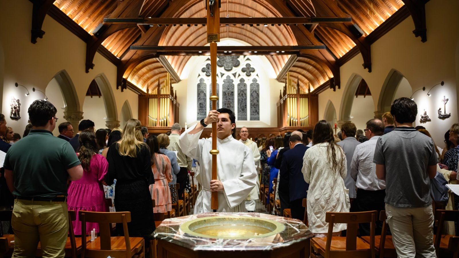 Young man holds cross while processing out of a chapel