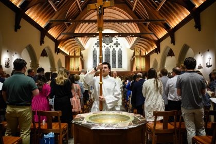Young man holds cross while processing out of a chapel