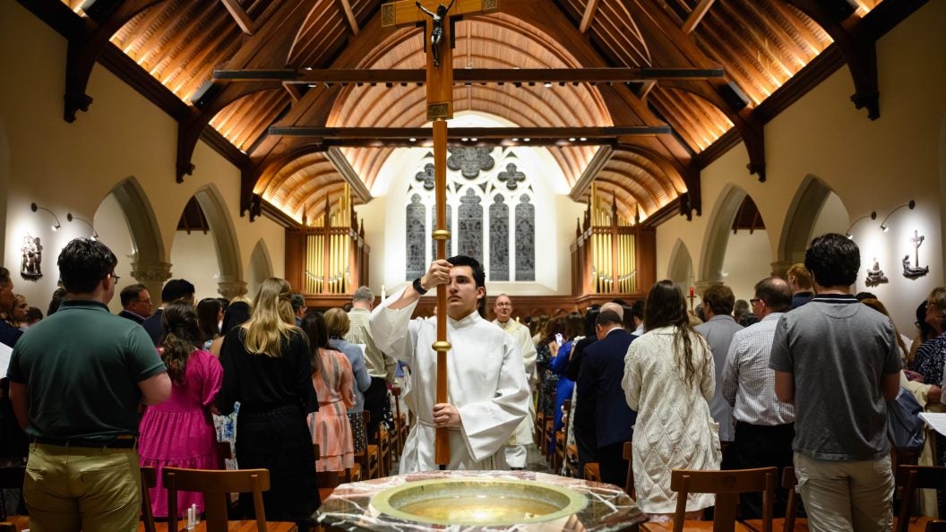 Young man holds cross while processing out of a chapel