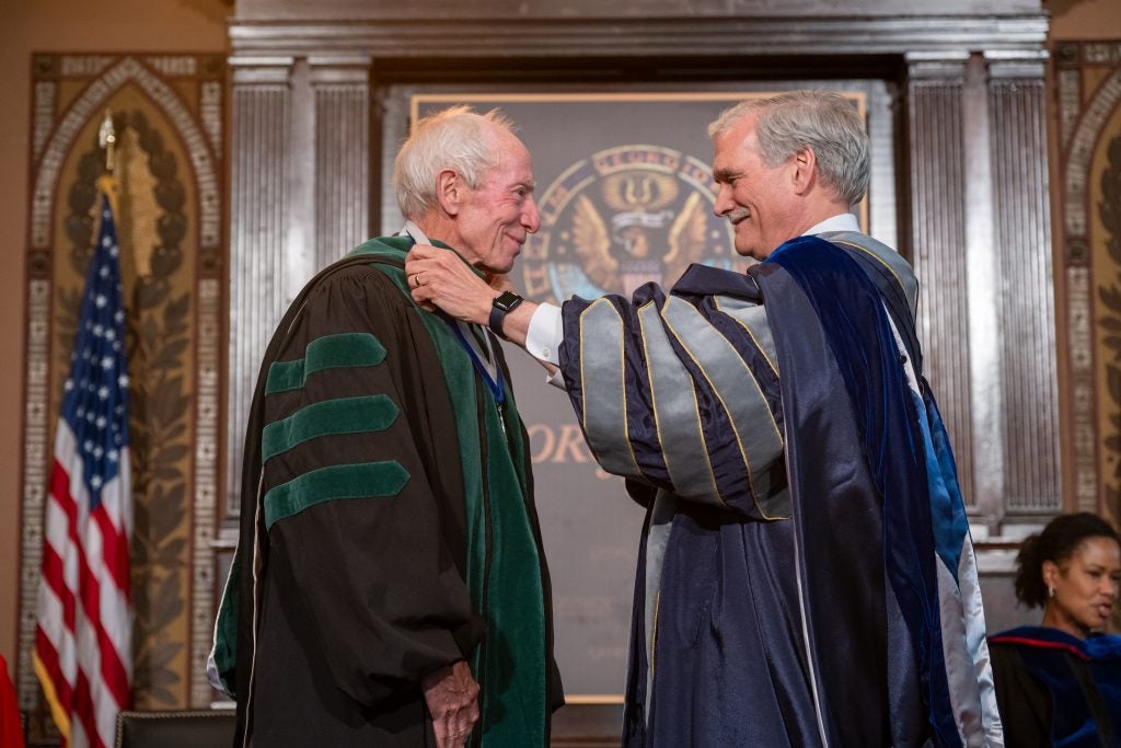 The interim president of Georgetown places a medal around a professor's neck. Both are dressed in academic robes