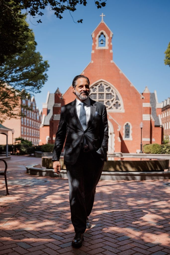 Incoming President Eduardo Peñalver steps across the courtyard of Dahlgren Quad on a sunny spring day. Behind him is a bright blue sky and a chapel