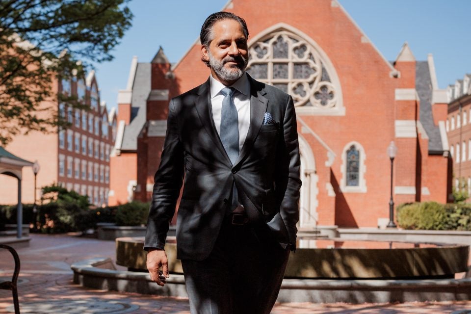 Incoming President Eduardo Peñalver steps across the courtyard of Dahlgren Quad on a sunny spring day. Behind him is a bright blue sky and a chapel
