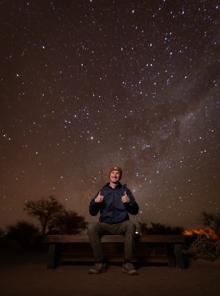 Young man giving thumbs up with a night starry sky behind him