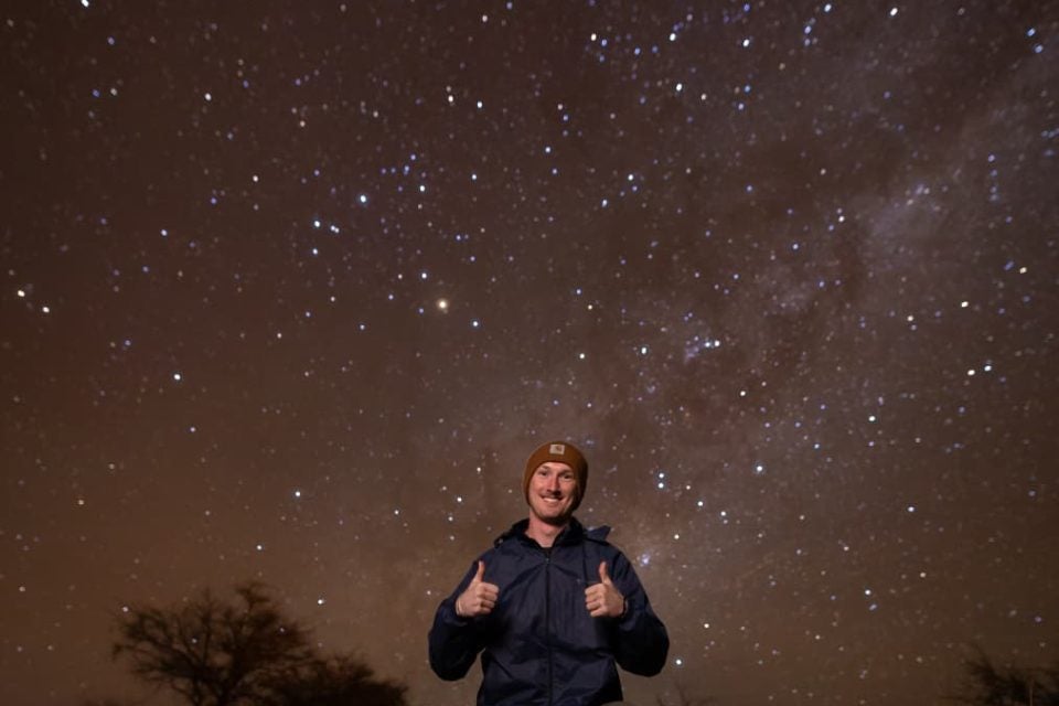 Young man giving thumbs up with a night starry sky behind him