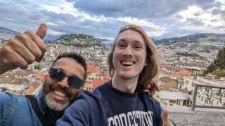 Young man takes selfie with another man overlooking a city