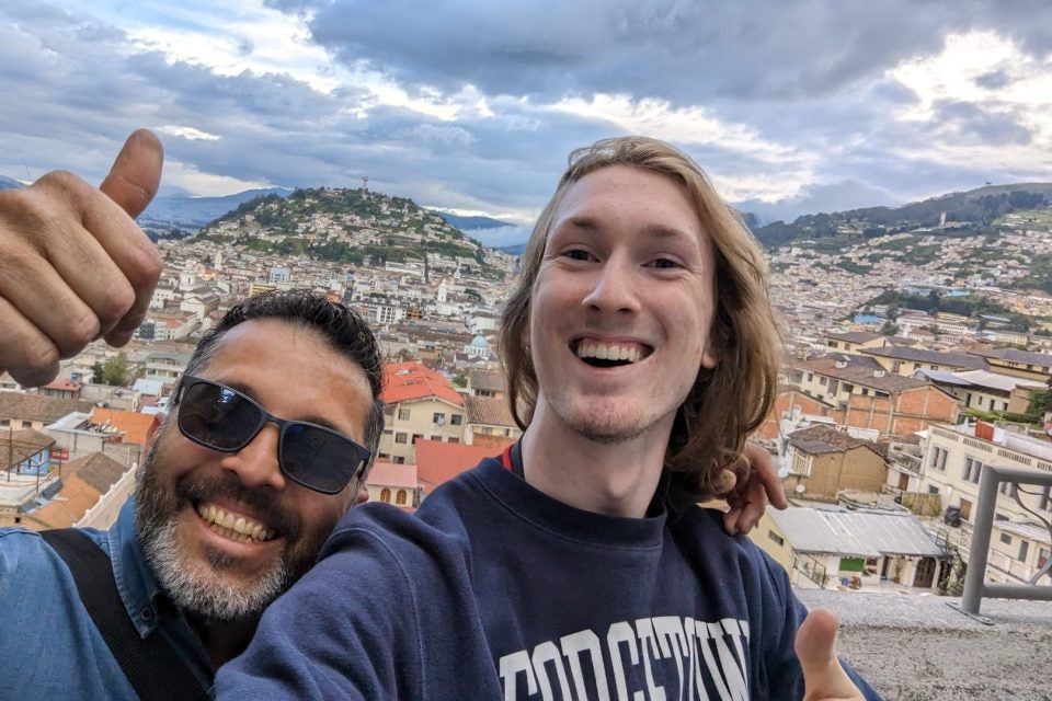 Young man takes selfie with another man overlooking a city