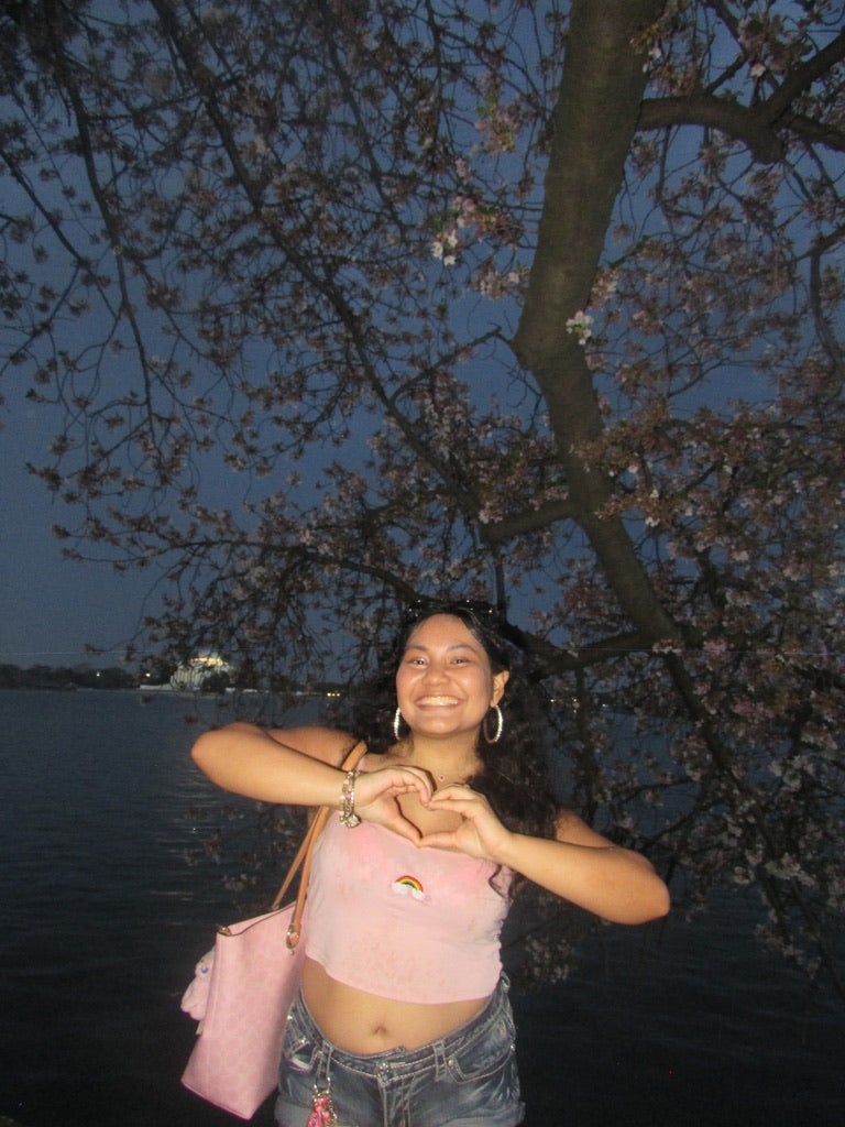 Young woman in pink shirt creates a heart with hands at cherry blossoms
