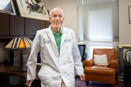 A doctor in a white lab coat smiles in front of a desk