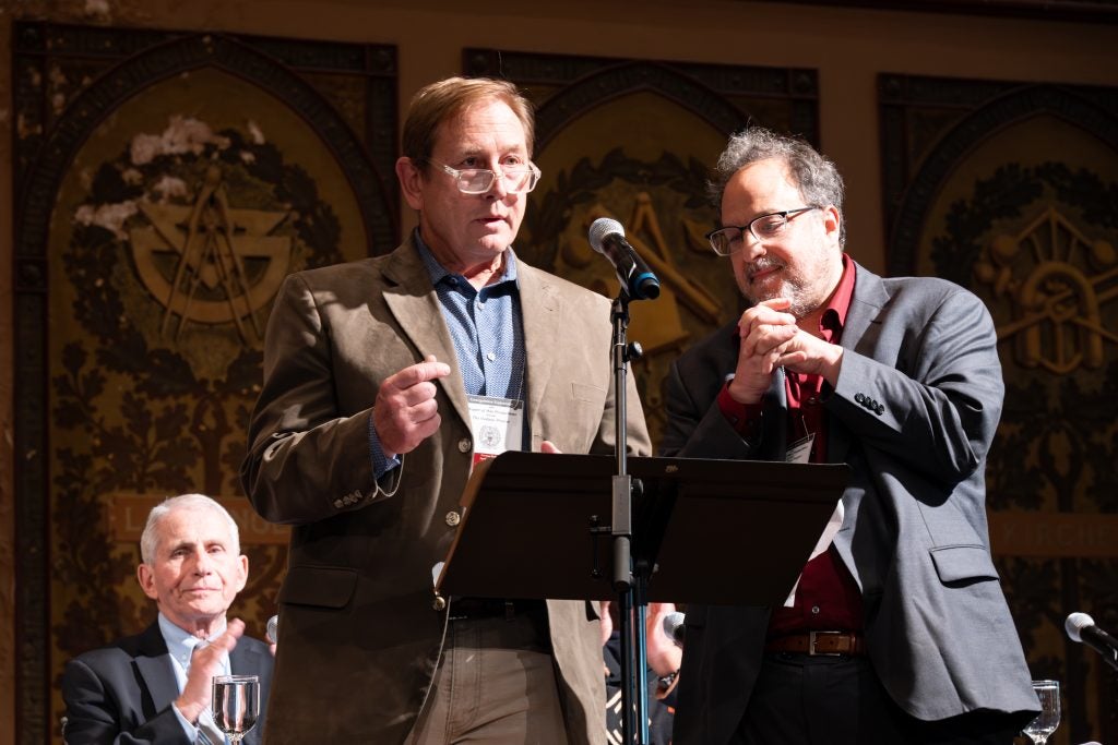 Two men speak at microphone on stage