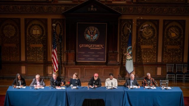 A panel on stage in Gaston Hall during performance