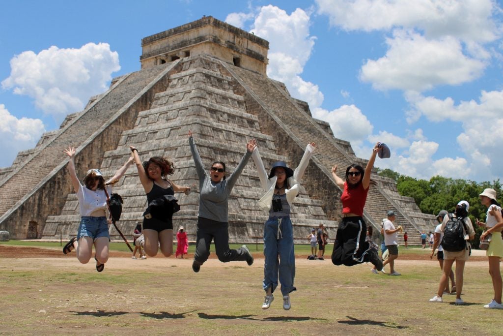 Group of students jump up in front of a pyramid in Mexico