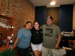 A daughter smiles between her parents in a dorm room