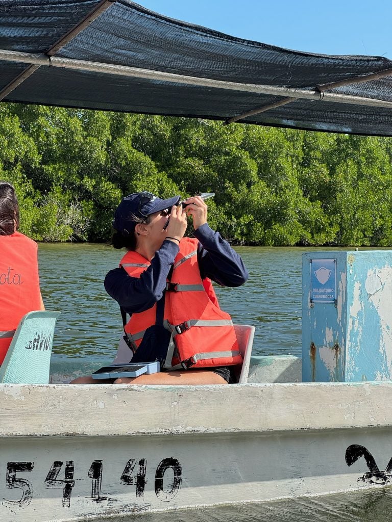 A woman in a life vest using a scientific instrument while on a boat