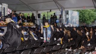 A senior in college smiles in a graduation cap and gown on her graduation day