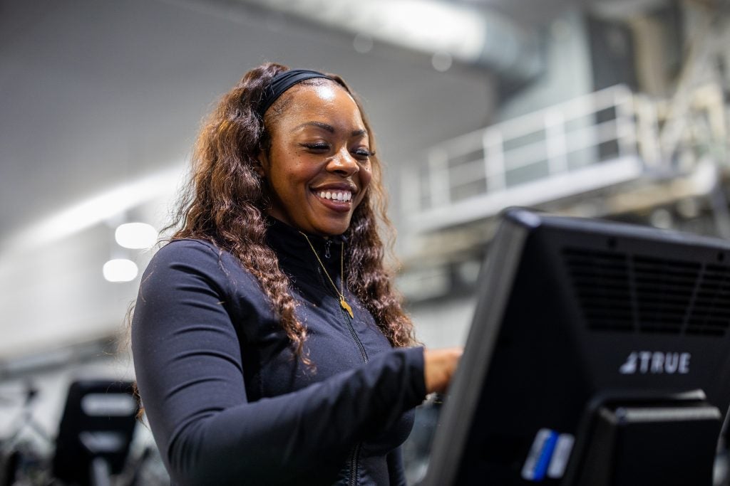 A woman smiles while tapping the touchscreen of a treadmill at a gym
