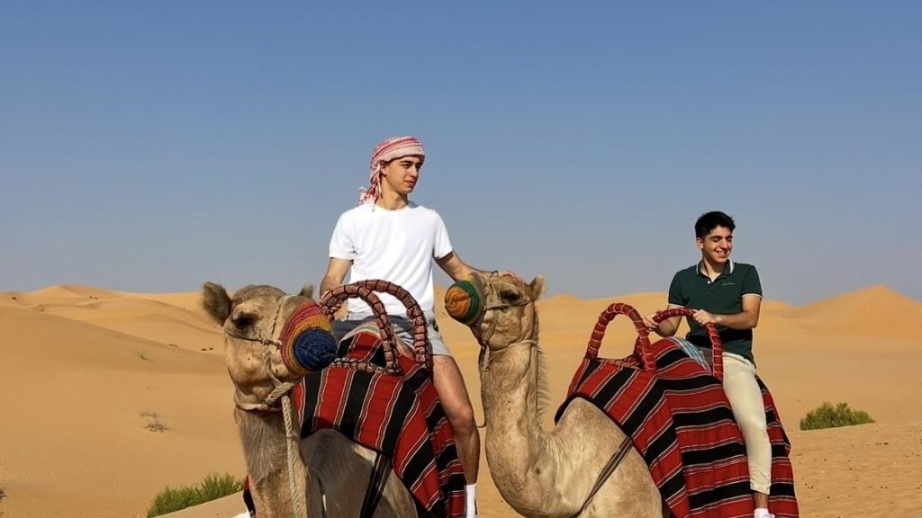 Two young men ride camels in the desert