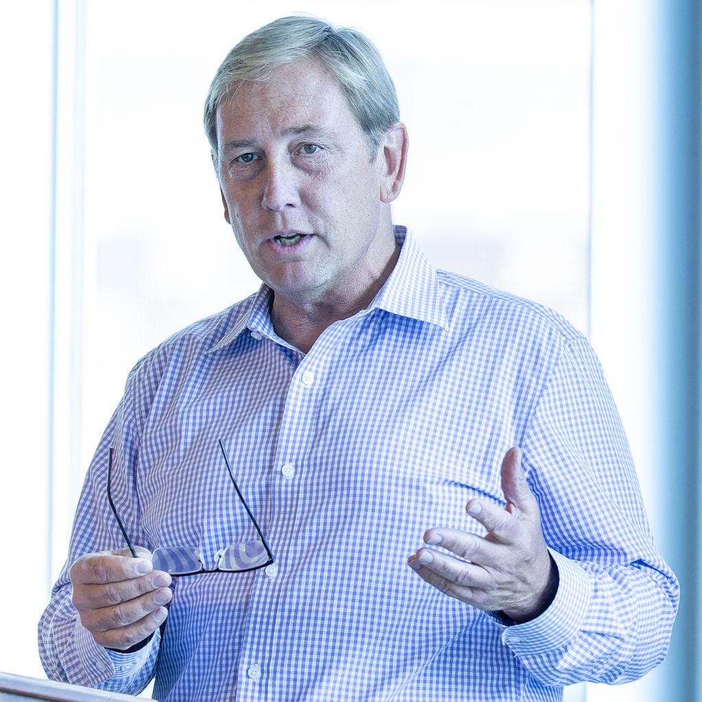 Peter Marra in a buttoned shirt speaking while holding glasses
