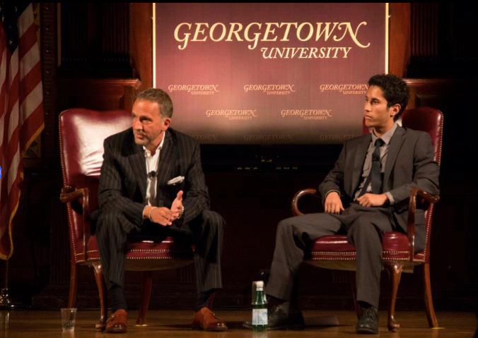 A student interviews an author on a Georgetown stage. They are both dressed in suits