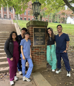 A group of medical students pose around a brick pillar outside an academic building