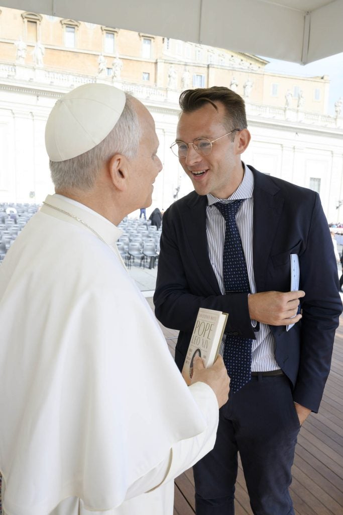 Pope Leo holds a book while a man smiles at him