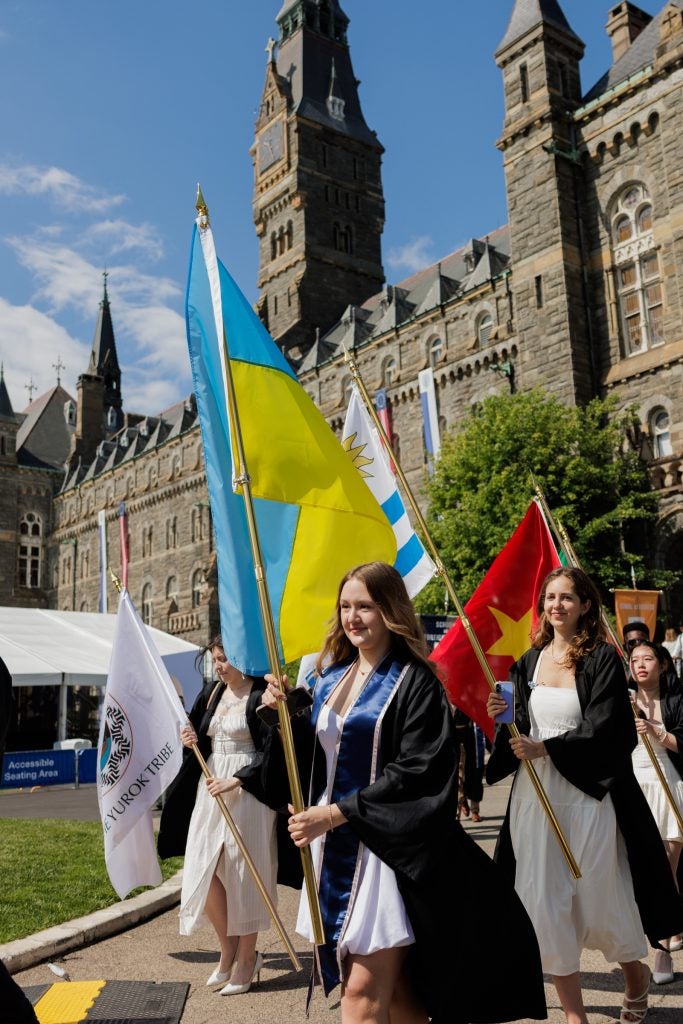 Young woman carries Ukrainian flag while in graduation regalia and smiling