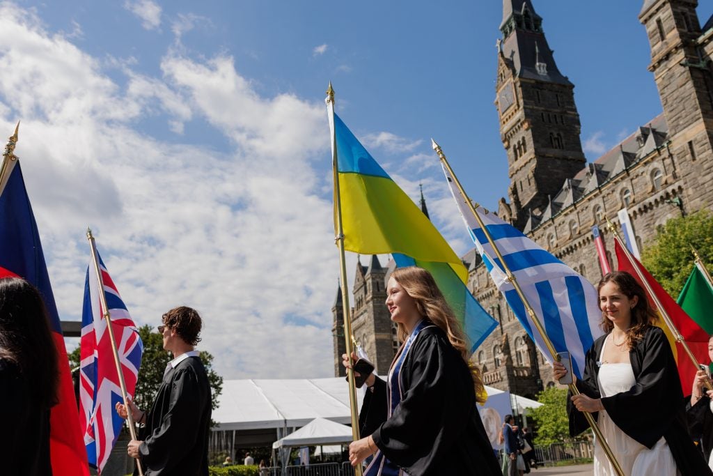 Young woman carries Ukrainian flag while in graduation regalia.