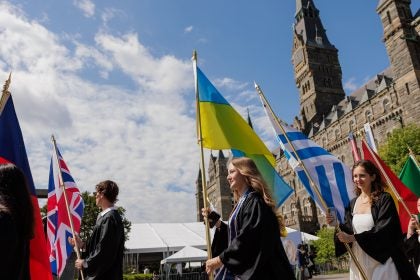 Young woman carries Ukrainian flag while in graduation regalia.
