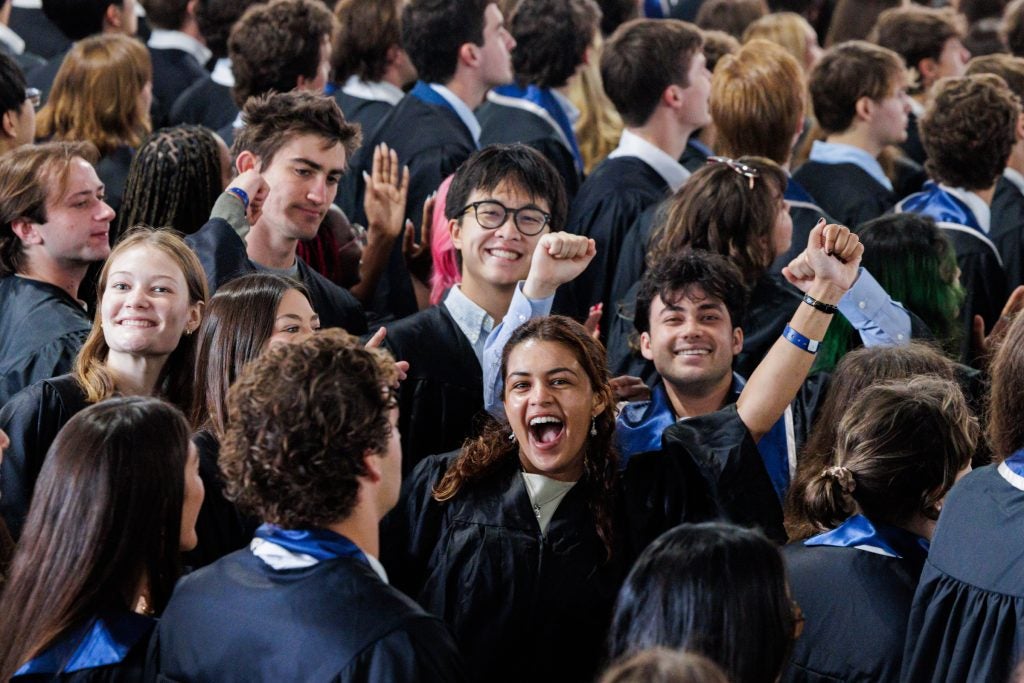 Students fist-bump in a crowd while wearing graduation gowns