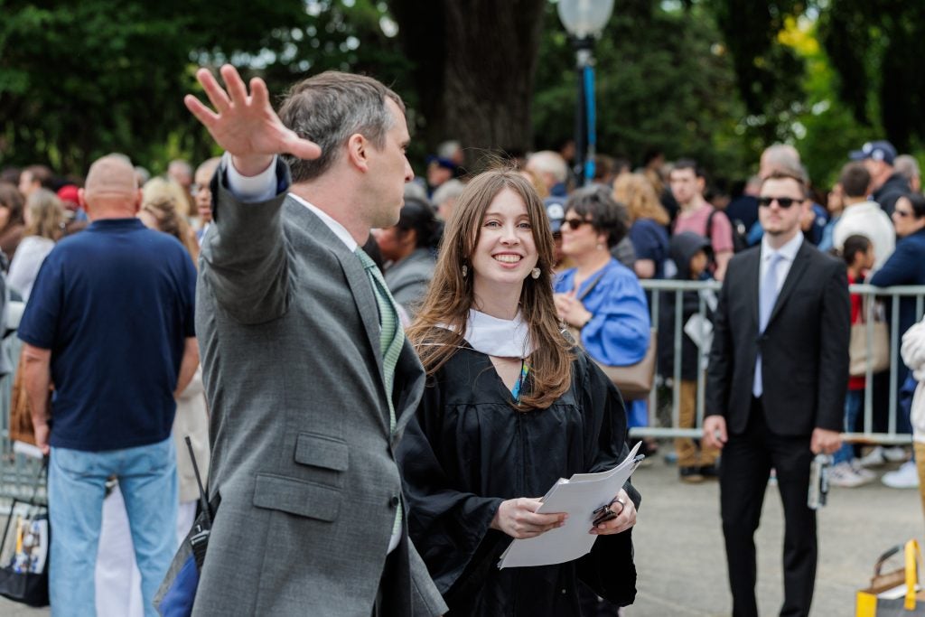 A woman in a graduation gown smiles while walking in a crowd