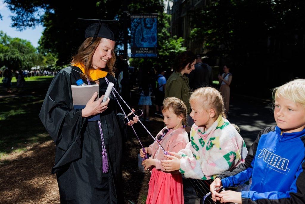 Two young girls pull on the tassels of a female graduate's graduation gown