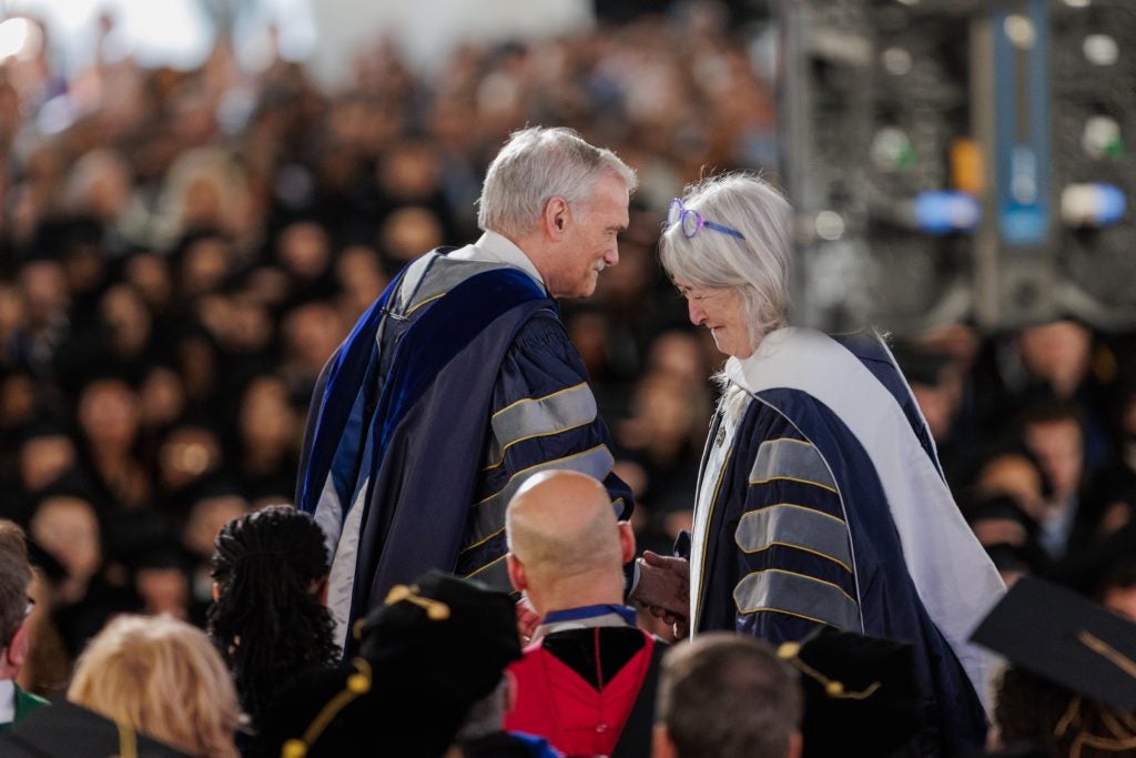 Interim President Groves smiles at a commencement speaker. Both are in graduation gowns.