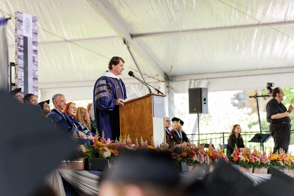Man in grad gown speaks to an audience on stage