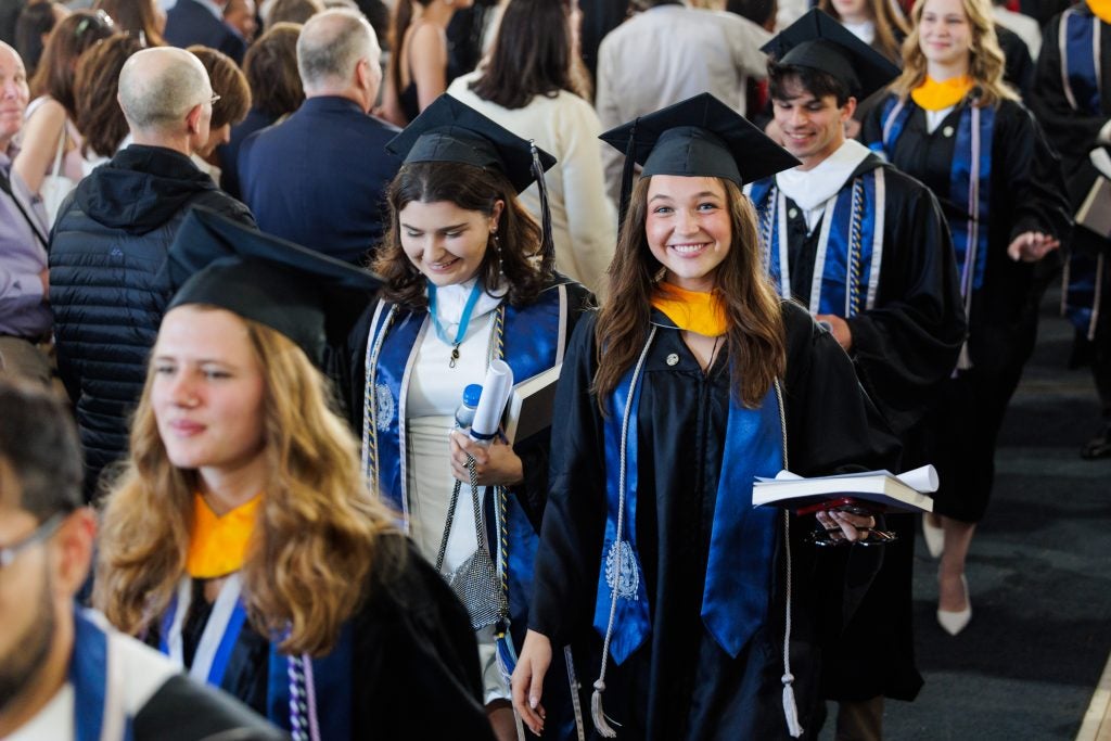 A female student in a graduation cap and gown smiles while processing out of graduation